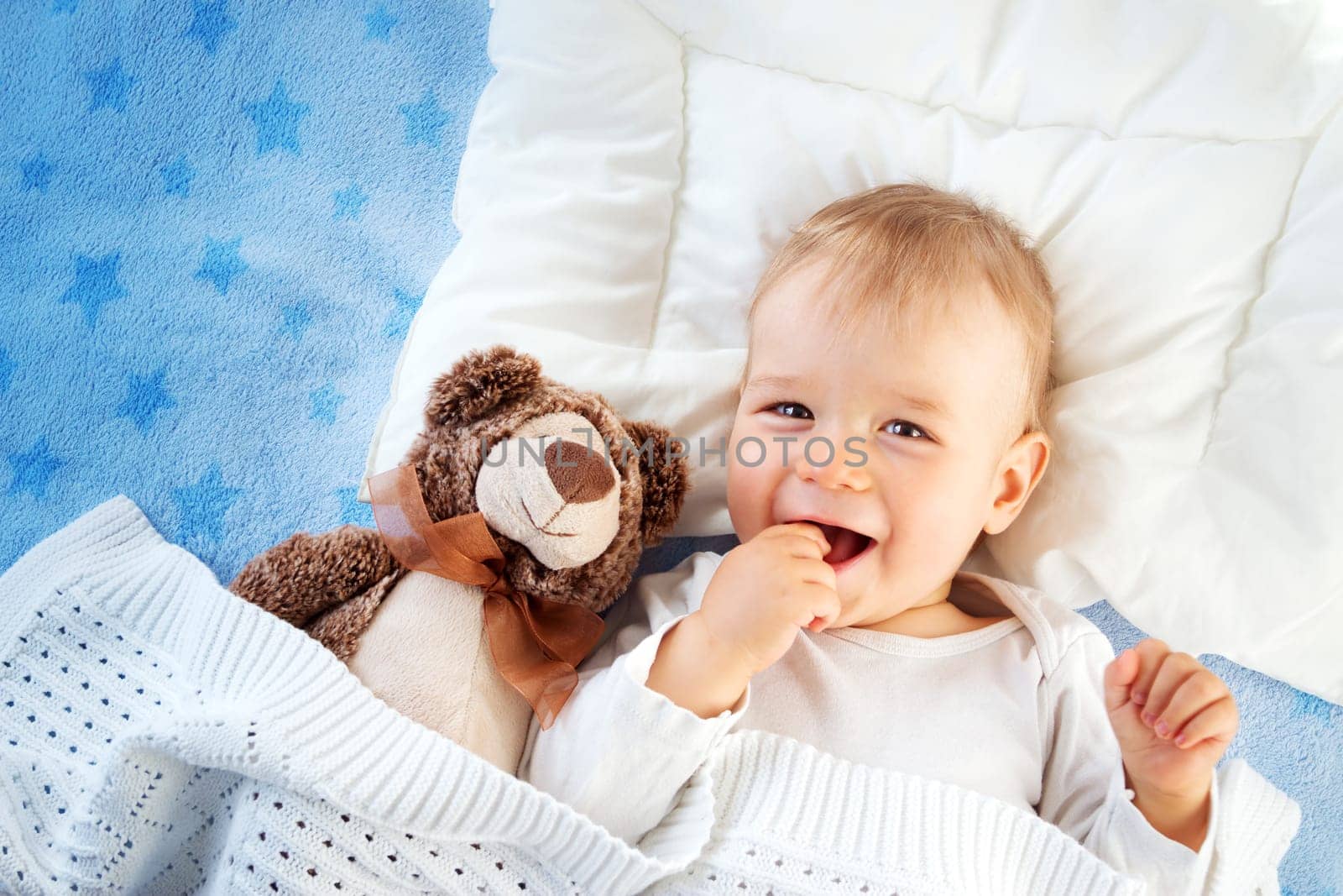 One year old baby lying in bed with a plush teddy bear