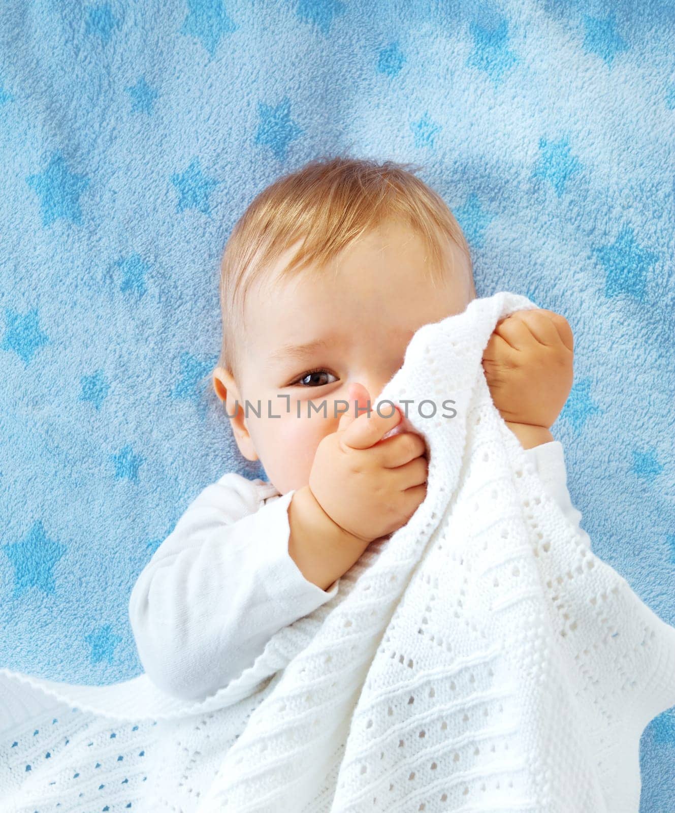 One year old baby lying on blue towel with stars. Child hiding under blanket