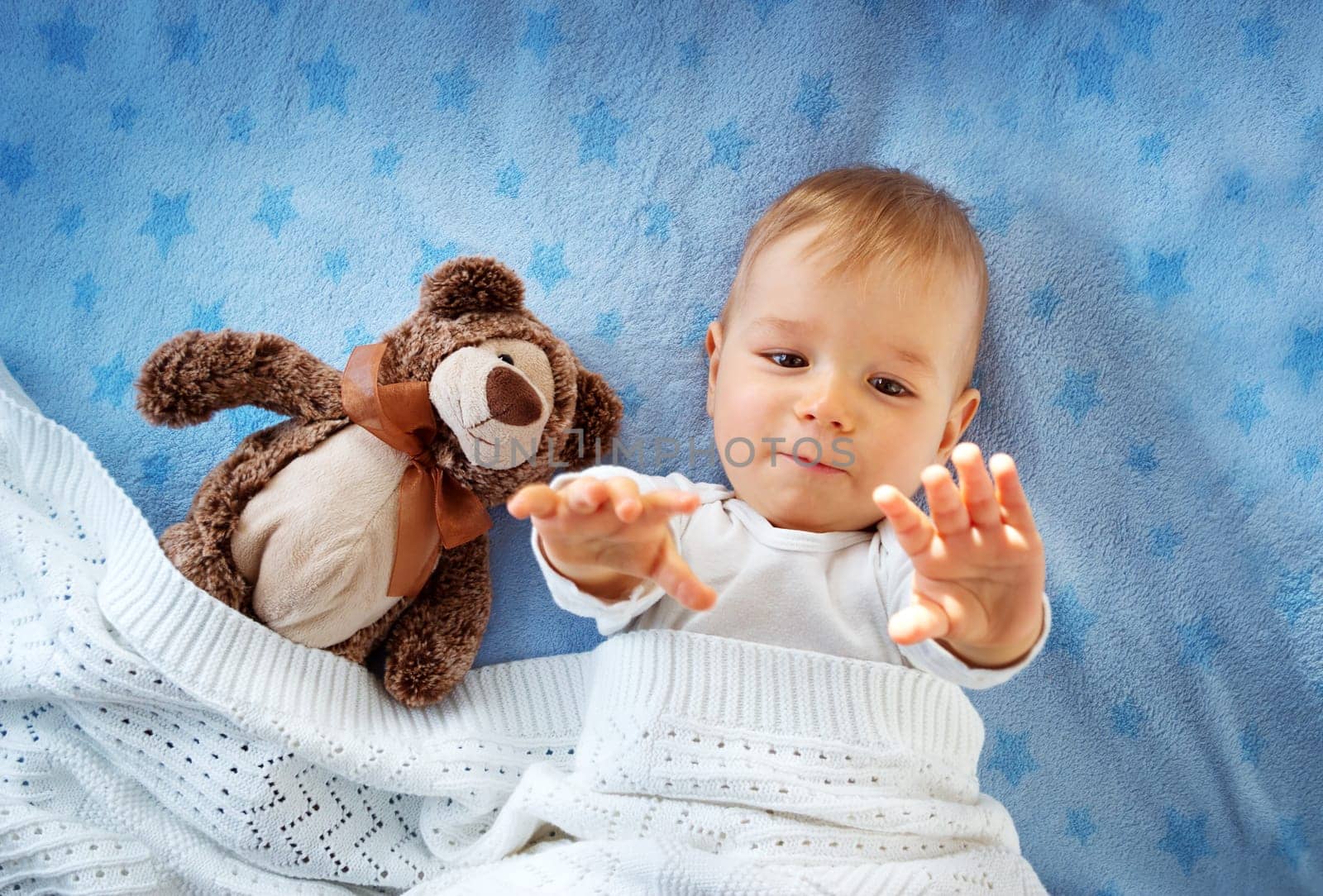 One year old baby lying in bed with a plush teddy bear