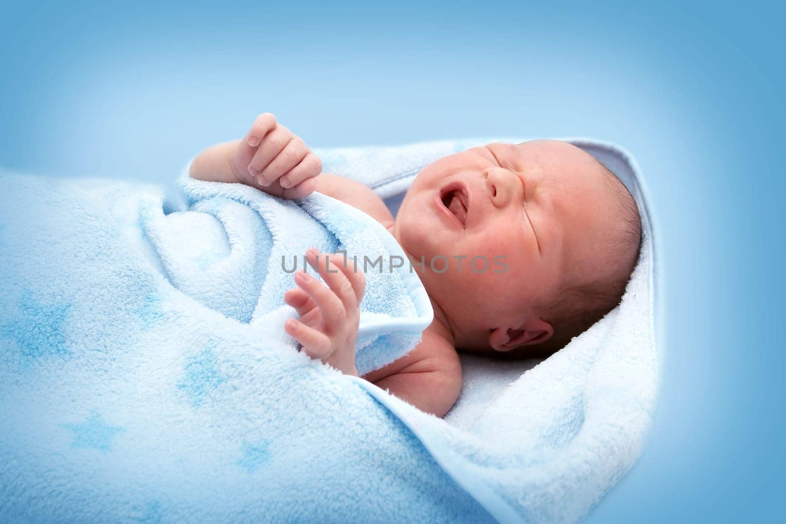 One week old crying baby in a blanket on blue background