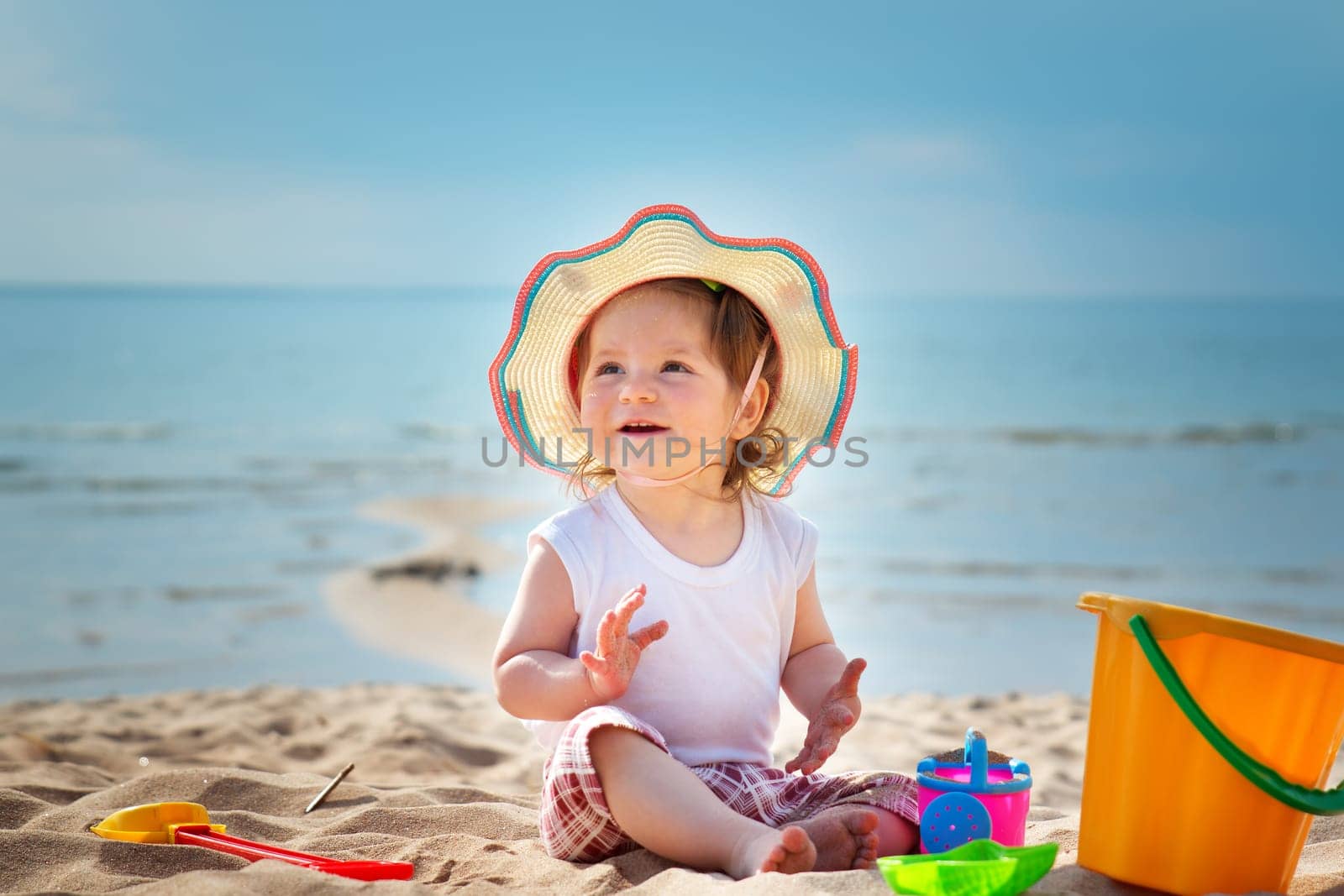 one year old girl shouting at the sea with bucket