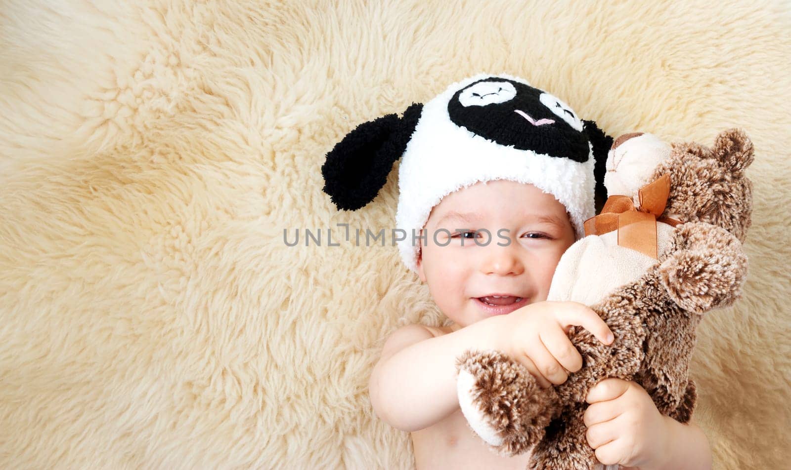 sleepy one year old baby lying in sheep hat on lamb wool background