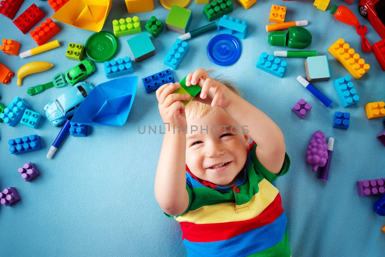 Baby boy lying on blue blanket with many toys around