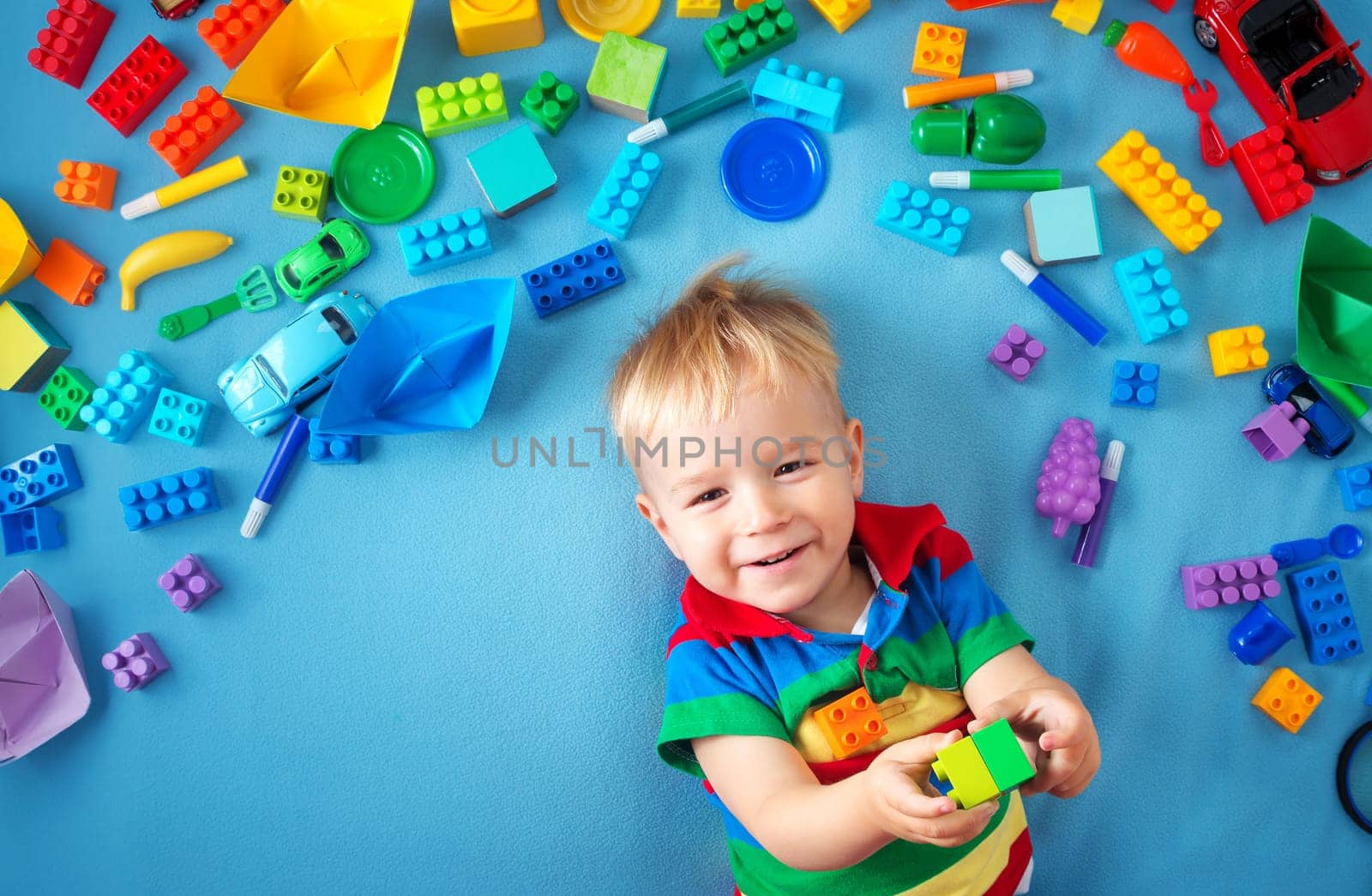 Baby boy lying on blue blanket with many toys around