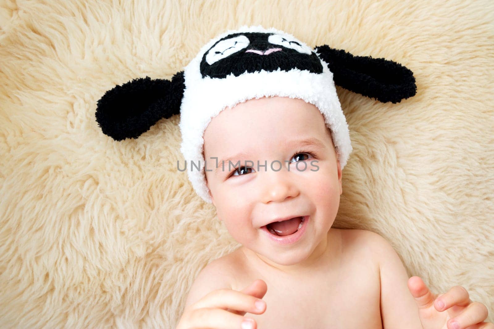 sleepy one year old baby lying in sheep hat on lamb wool background