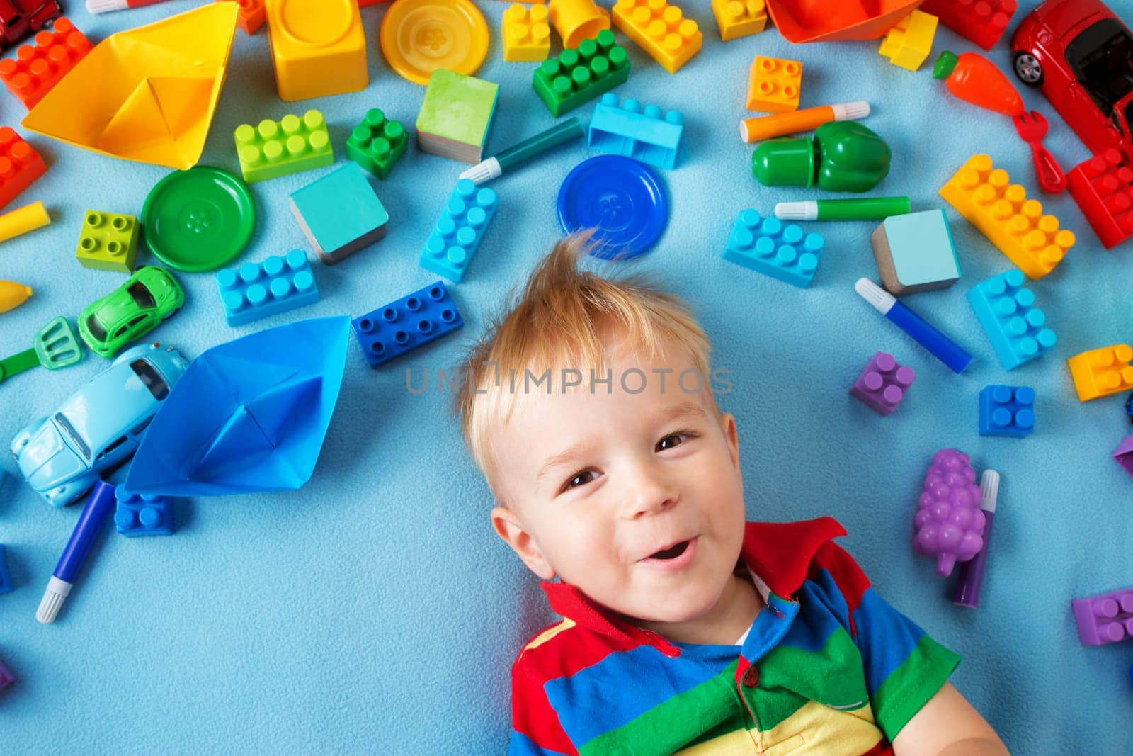 Baby boy lying on blue blanket with many toys around
