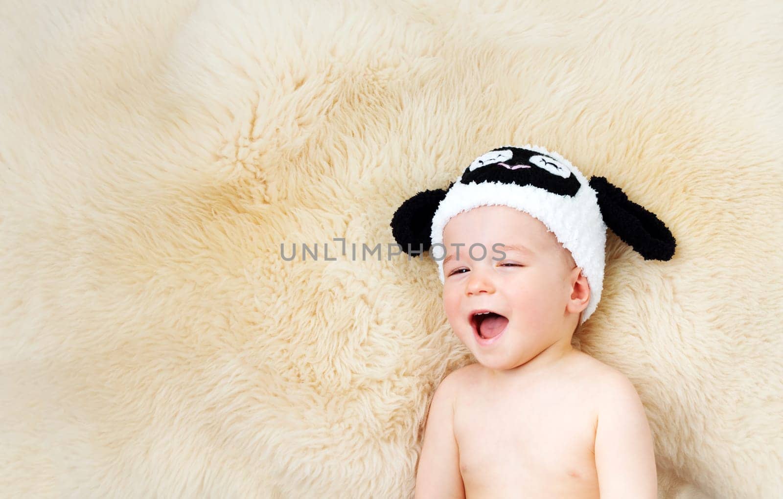 sleepy one year old baby lying in sheep hat on lamb wool background