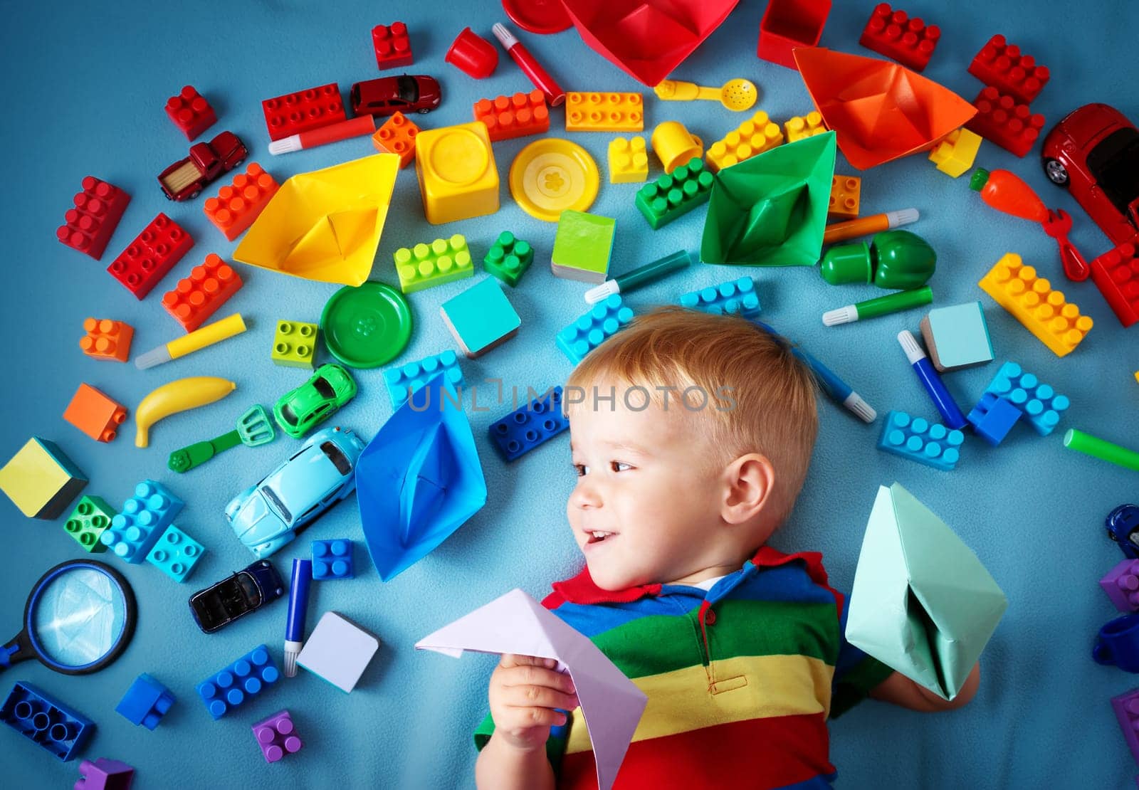 Baby boy lying on blue blanket with many toys around
