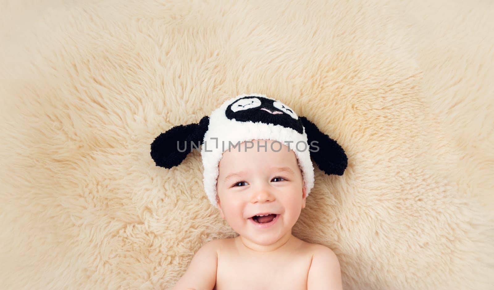 sleepy one year old baby lying in sheep hat on lamb wool background