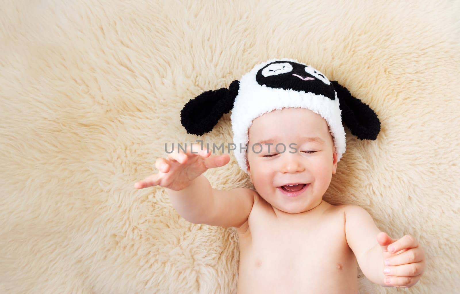 sleepy one year old baby lying in sheep hat on lamb wool background
