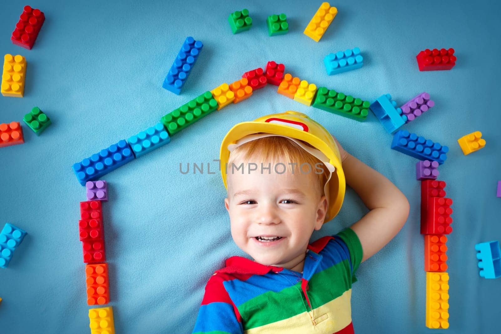Child lying on blue blanket with blocks in house shape
