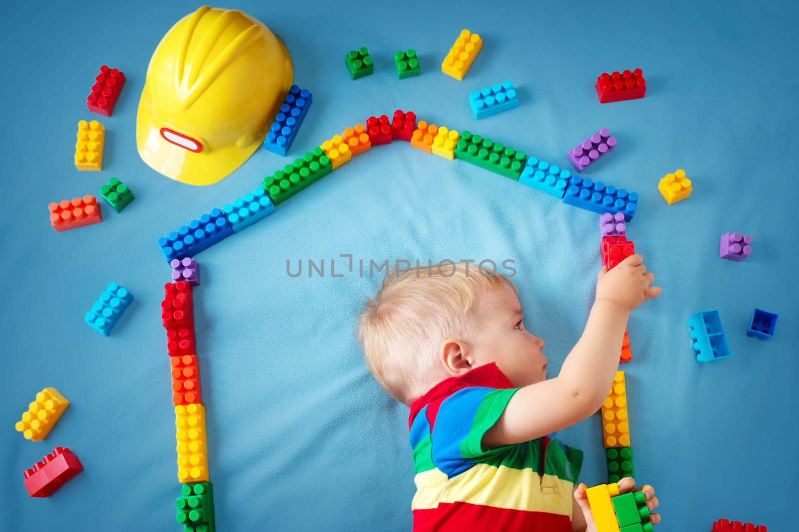 Child lying on blue blanket with blocks in house shape