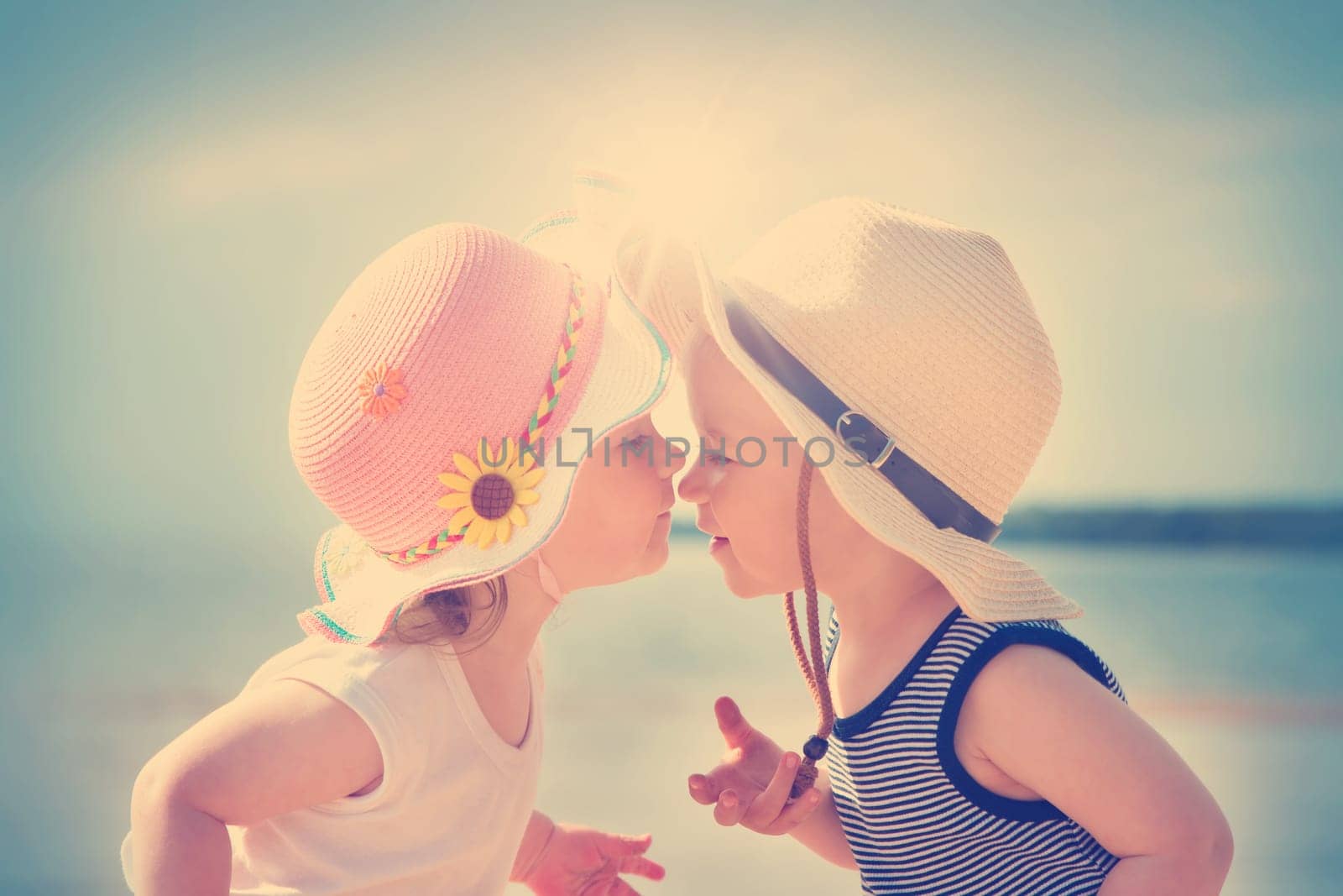 Babygirl and babyboy kissing on the beach in straw hats