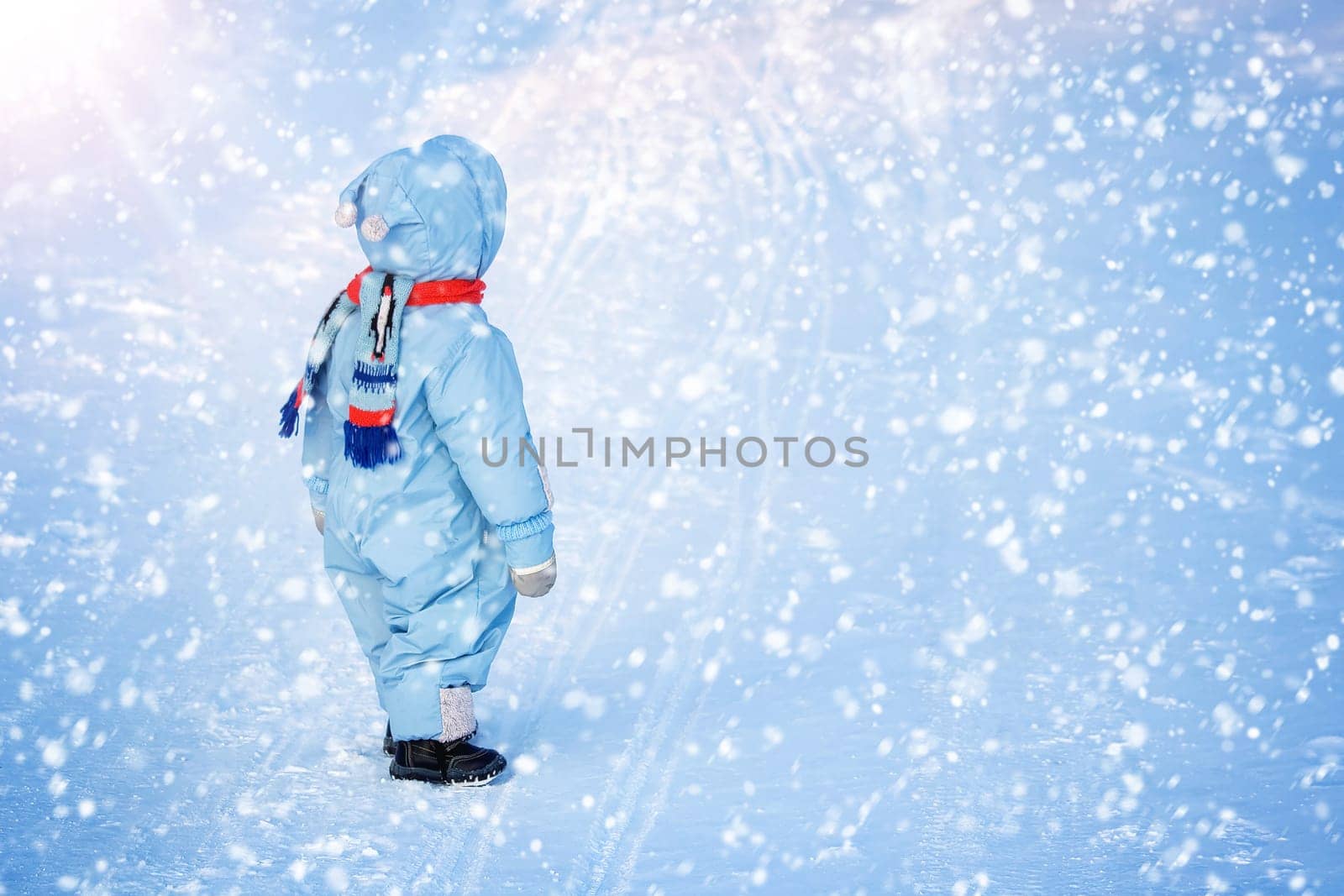 Baby boy at snowfall. Child in winter clothes