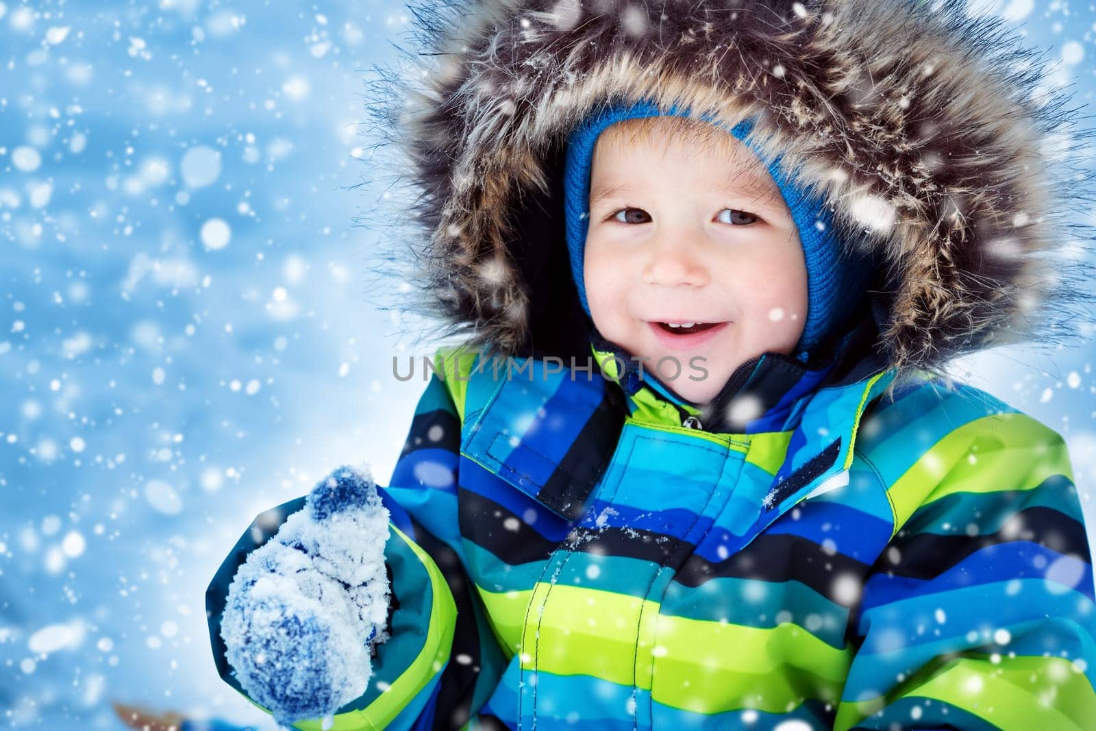 Baby boy smiling at snowfall. Child in winter clothes