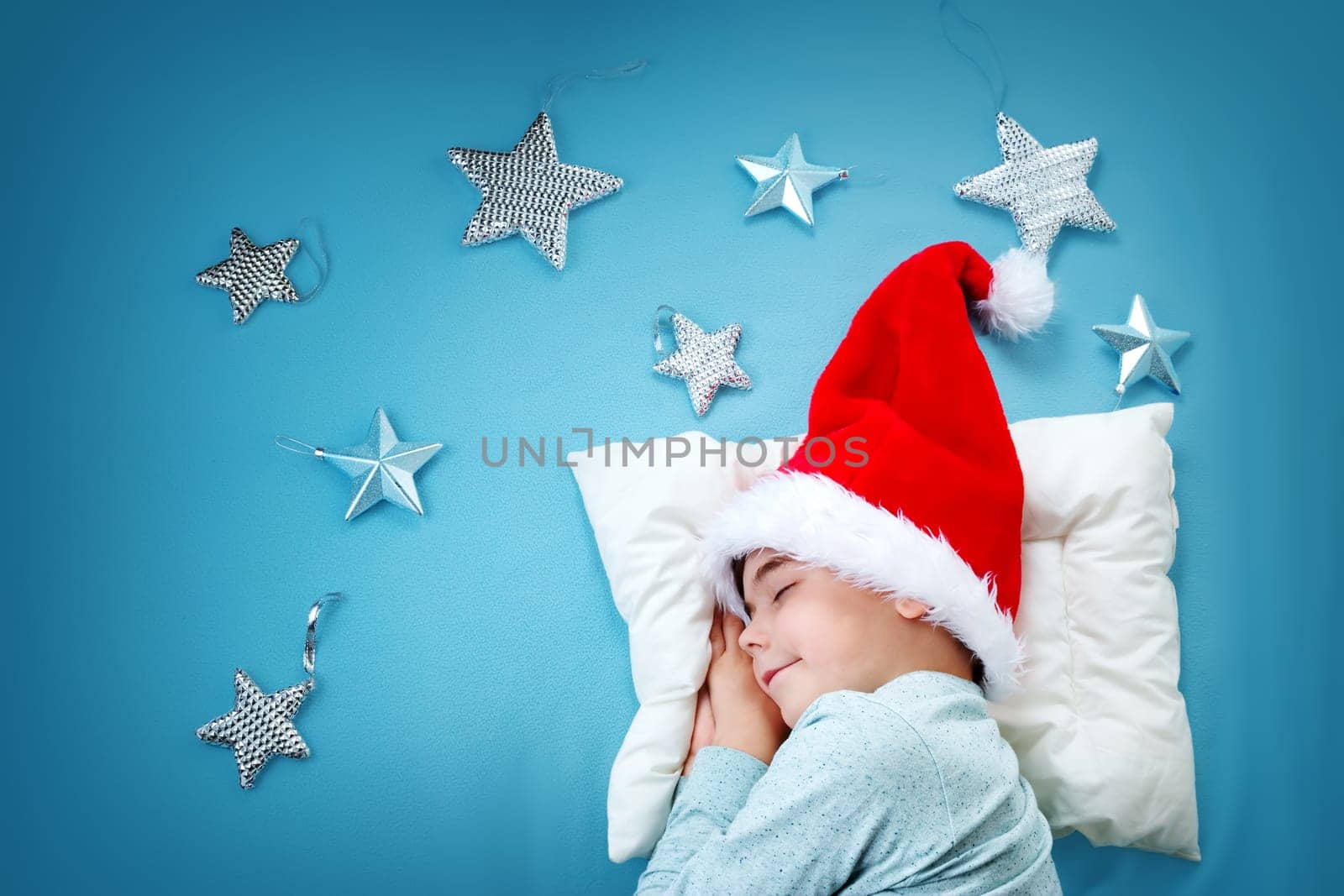 Sleepy child on blue blanket in red hat. Cute boy sleeping in christmas cap
