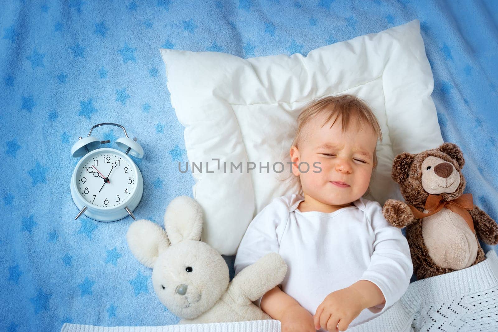 One year old baby lying in bed with alarm clock