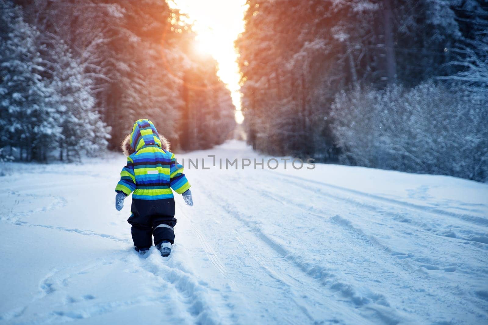 Baby boy walking at snowfall. Child in winter clothes playing with snow