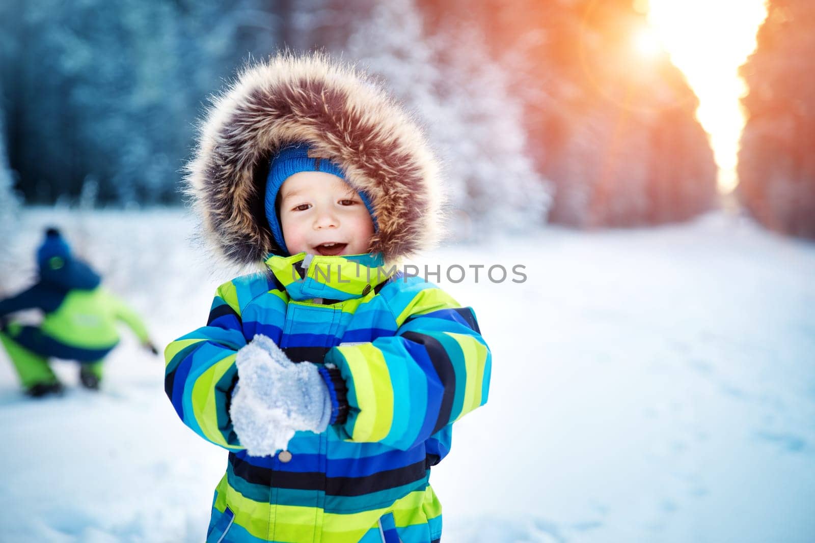 Baby boy walking at snowfall. Child in winter clothes playing with snow