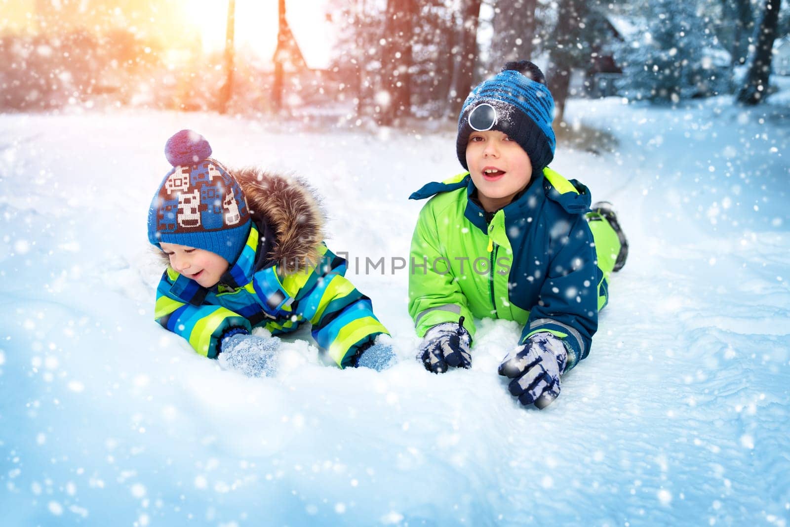 Children playing in snow at snowfall. Boys in winter clothes outdoors in cold weather