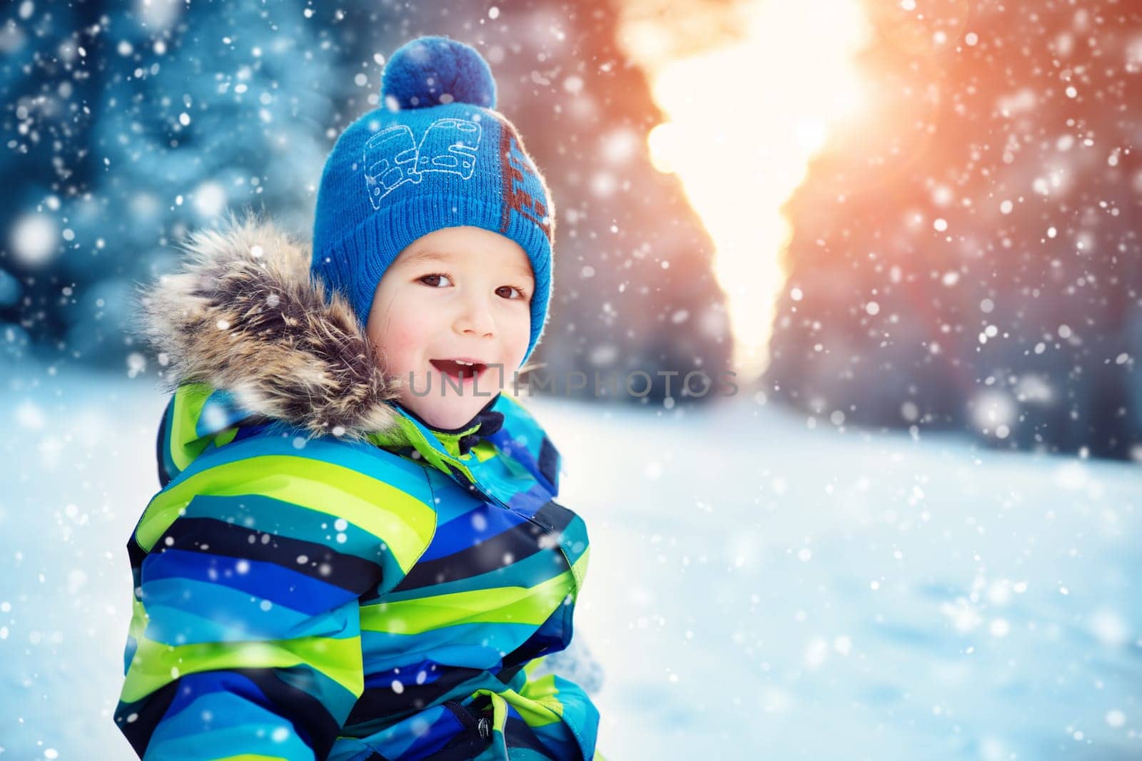 Baby boy walking at snowfall. Child in winter clothes playing with snow