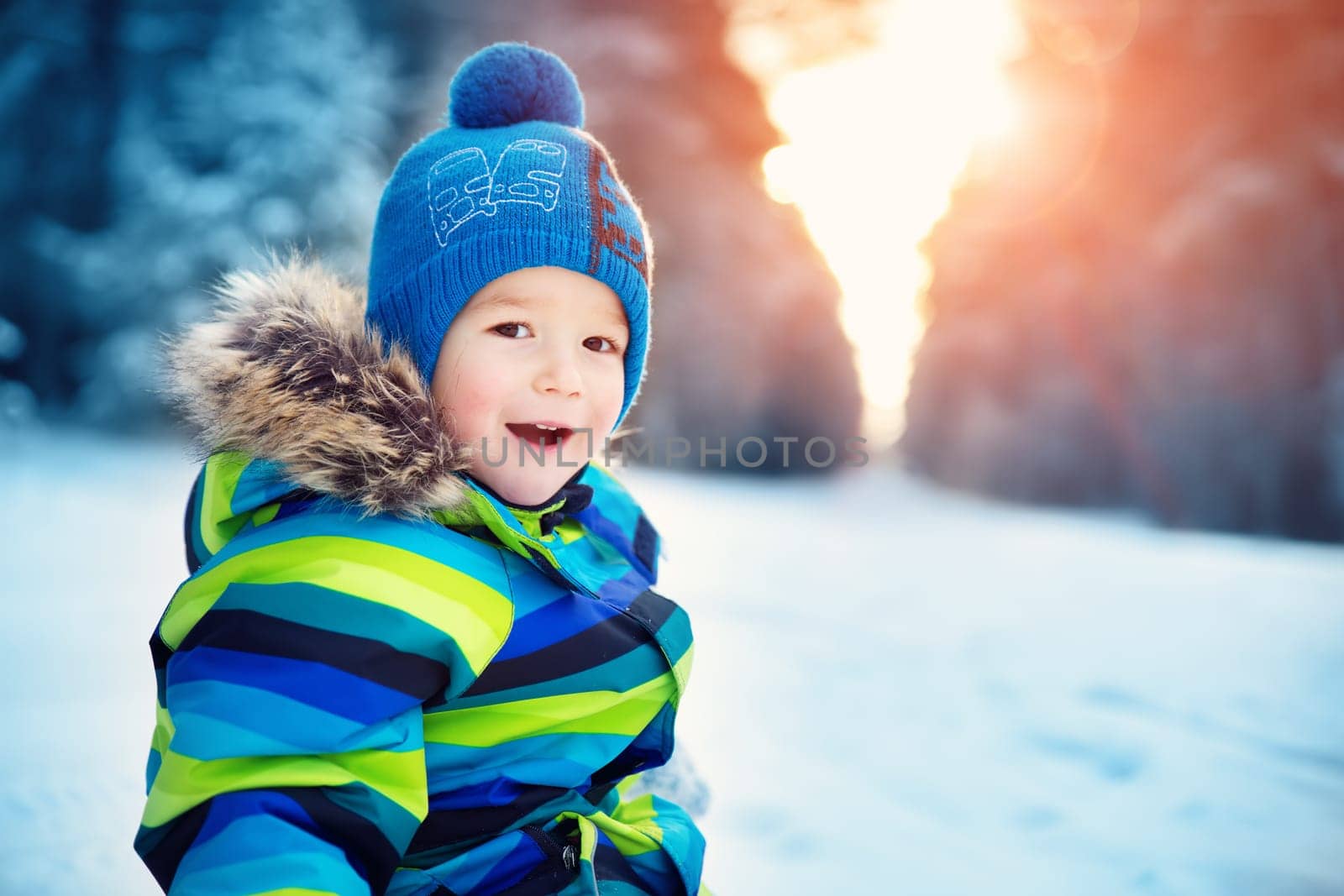 Baby boy walking at snowfall. Child in winter clothes playing with snow