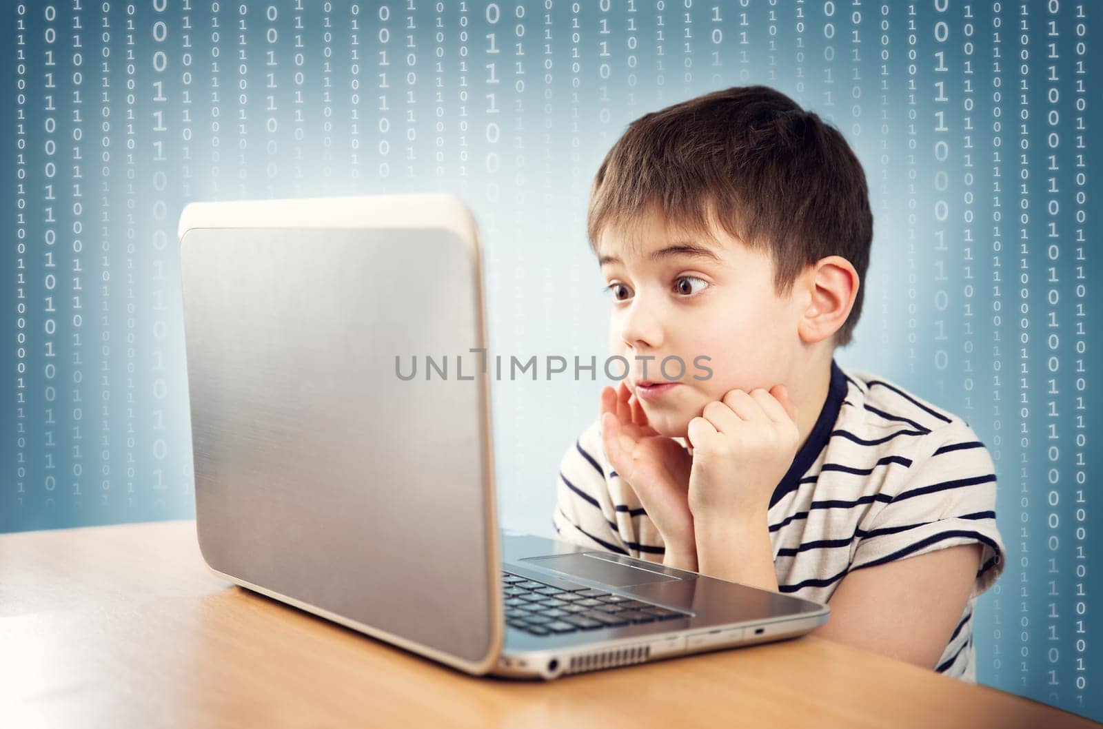 surprised seven years old child sitting with a laptop at table