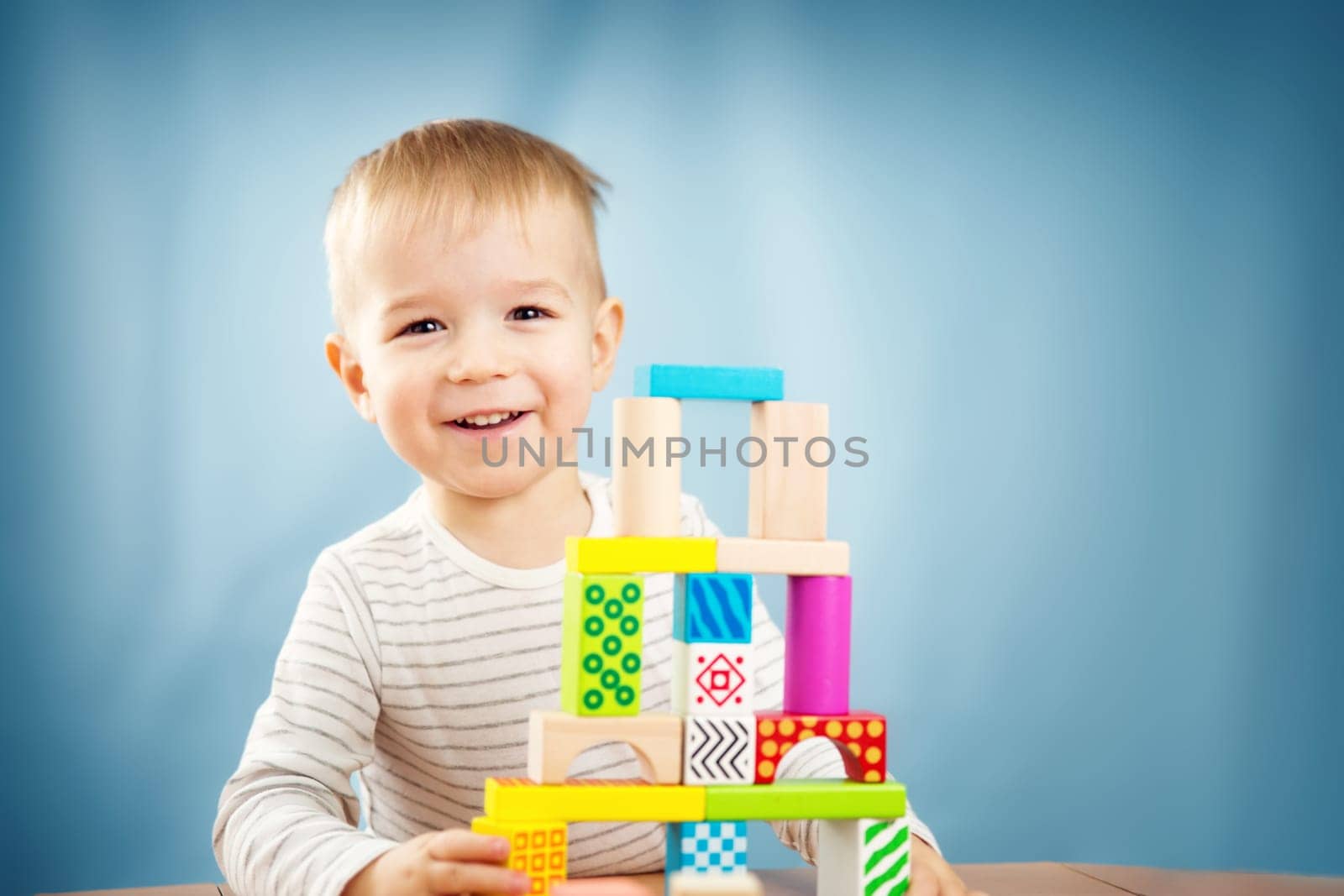 Portrait of a two years old child stacking wooden cubes. Pretty little boy on blue background