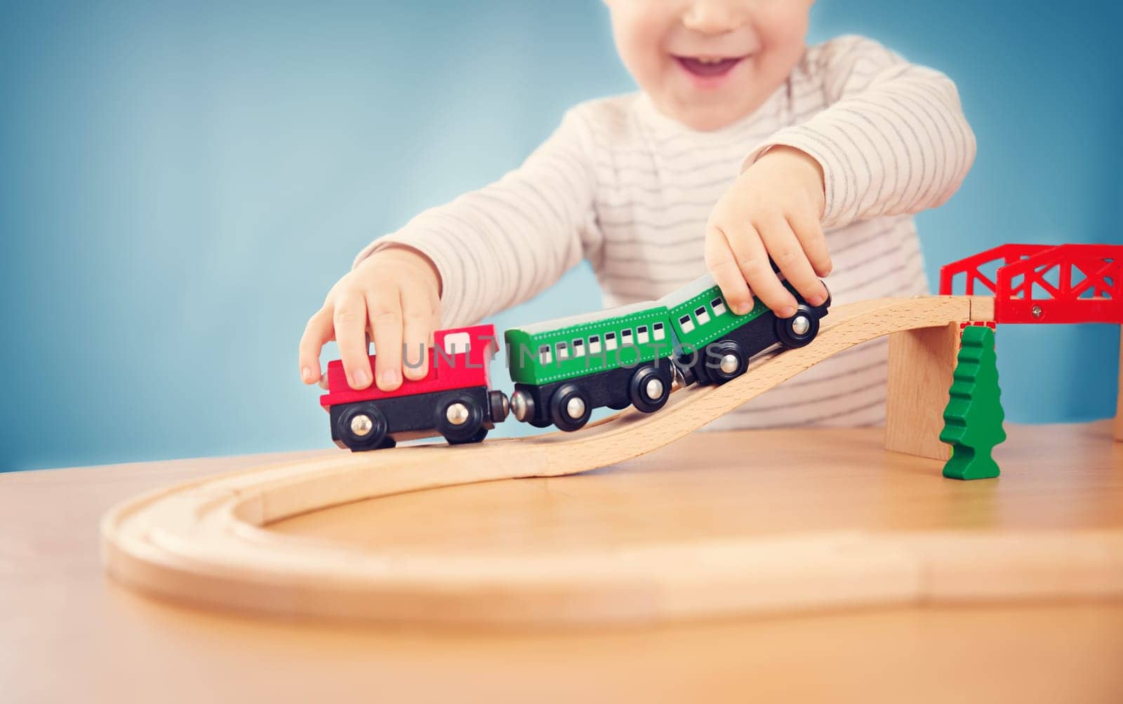 Portrait of a two years old child sitting at the table and playing with a railroad. Pretty little boy on blue background