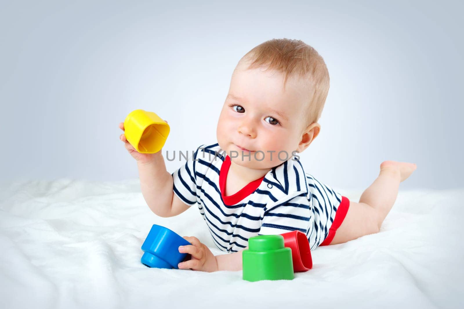 Nine month old baby lying in the bed on white blanket. Cute boy playing with cubes