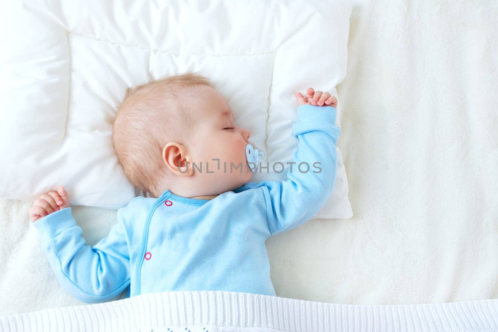 Seven month old baby sleeping on white blanket and pillow. Sleepy child on soft bedding with pacifier