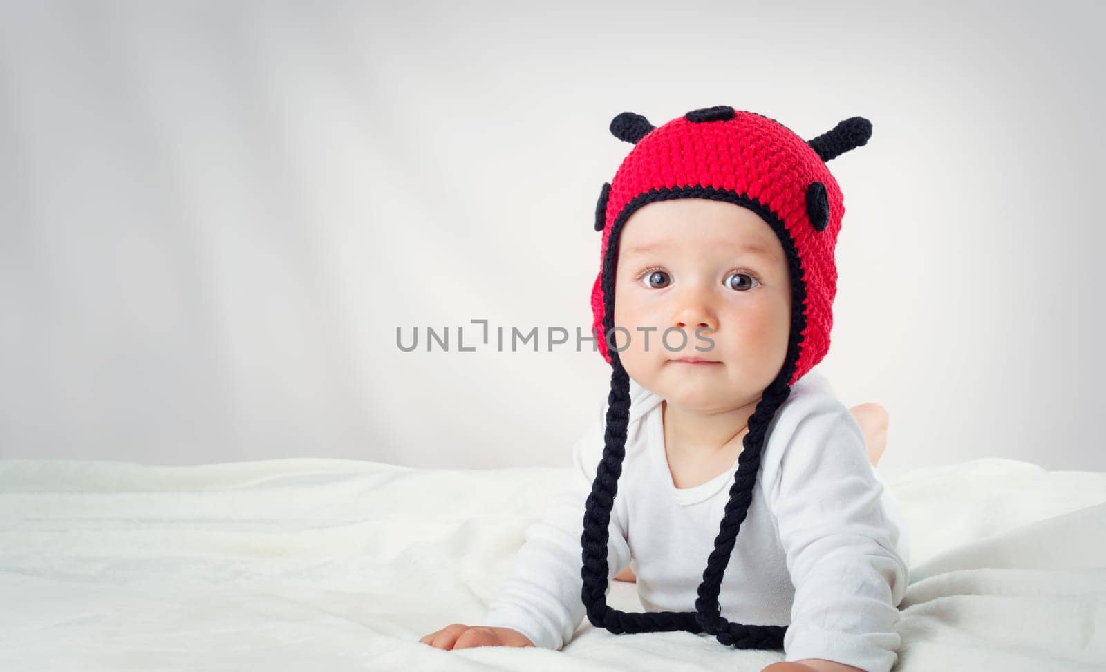 Cute baby lying in the bed on white blanket in knitted ladybug hat. Pretty little boy