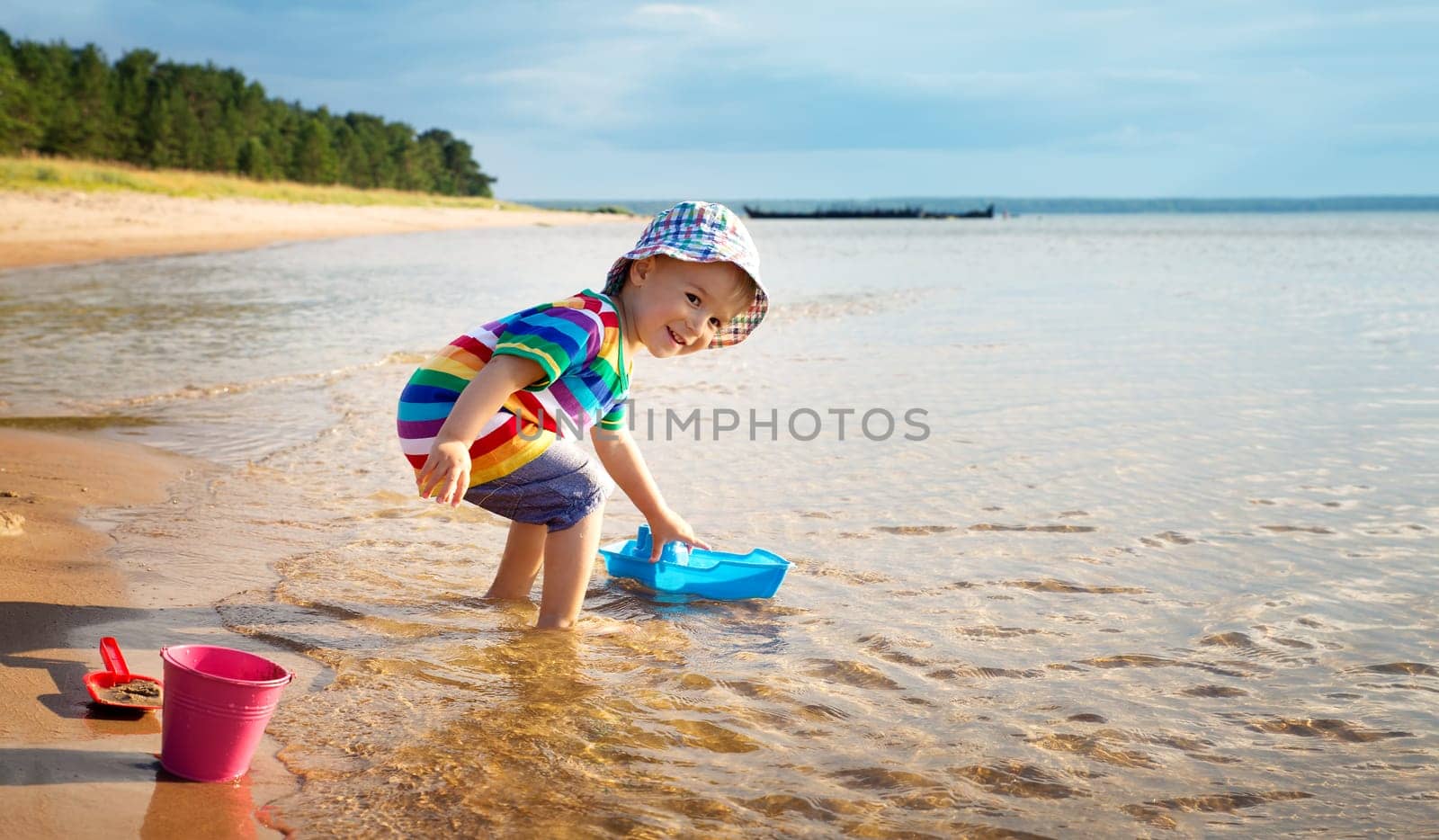 Baby boy playing with ship toy at sea. Child os on vacation in summer at the beach on vacations