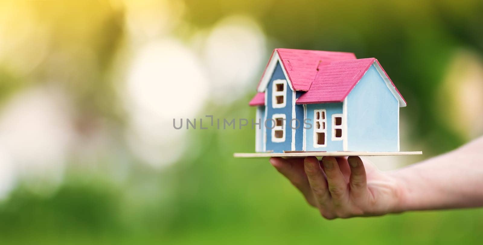 man hands holding wooden house on the grass