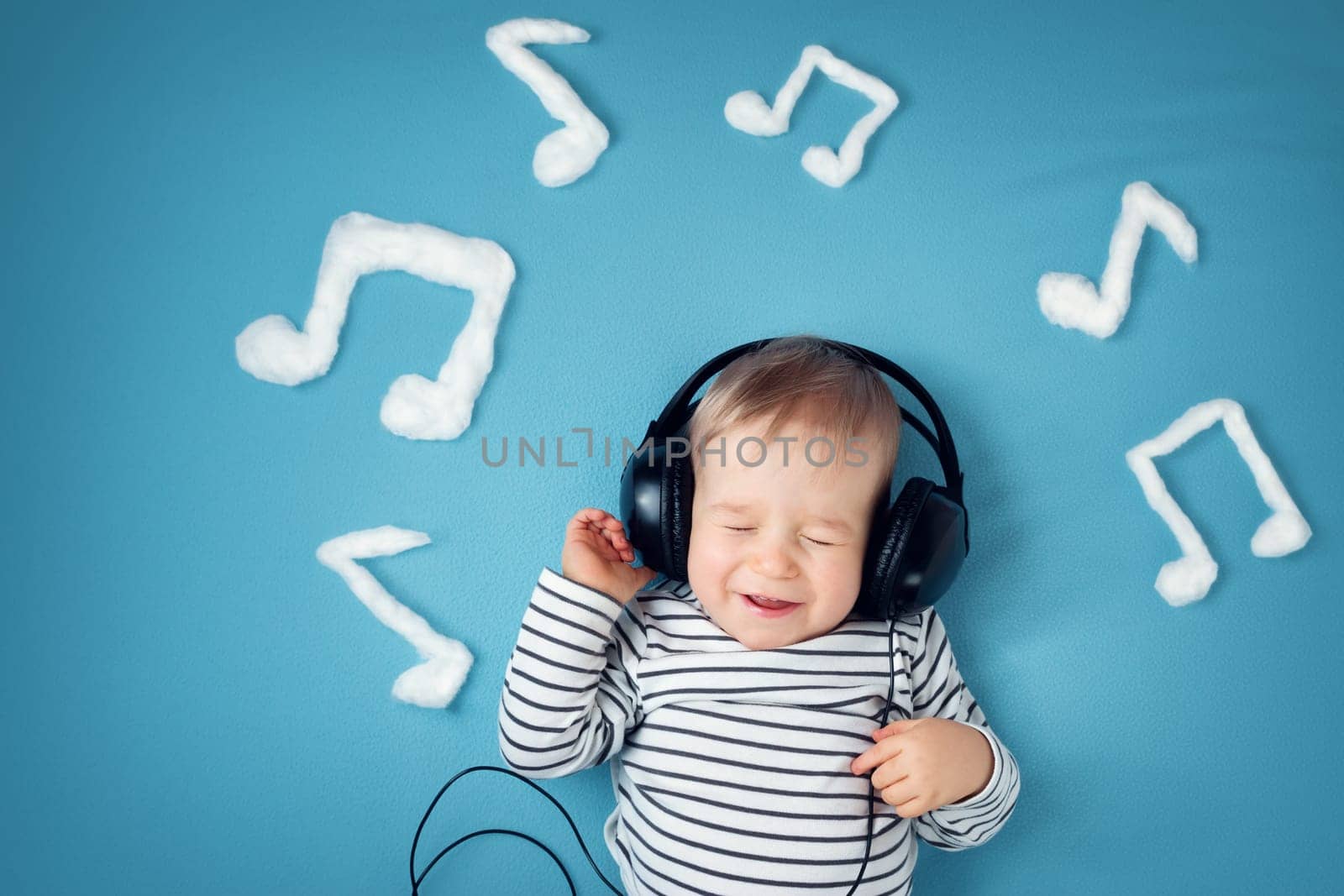 happy little boy on blue blanket background with headphones and musical notes on blue background