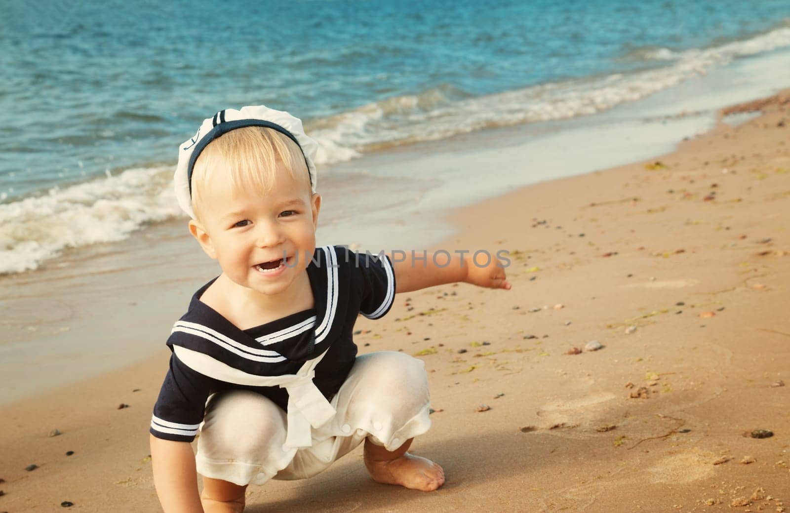 one year old boy walking at the beach in straw hat. Child on family vacations at sea
