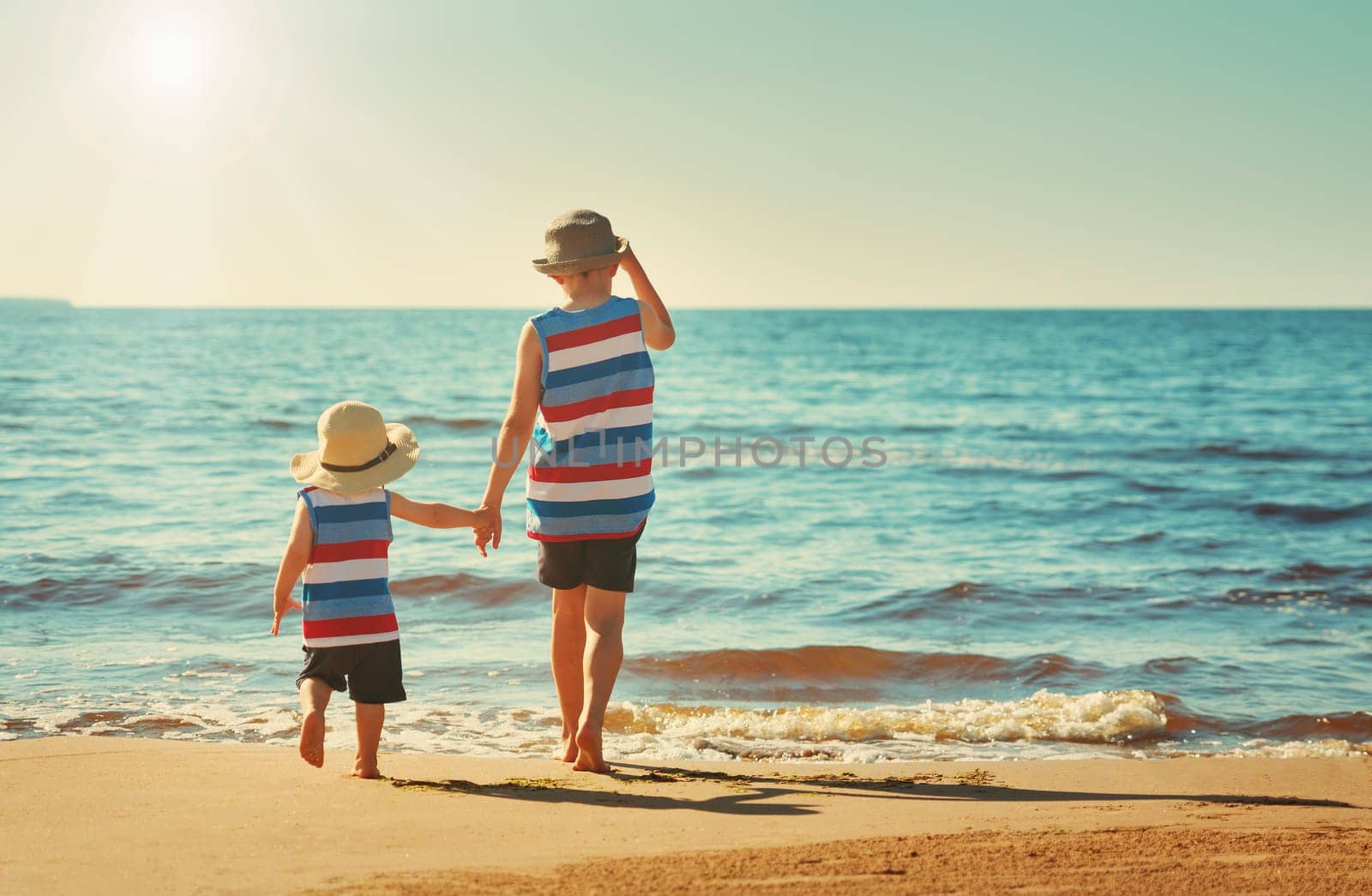 Two brothers barefoot are walking on the beach in water. Boys are on vacation in summer at the sea