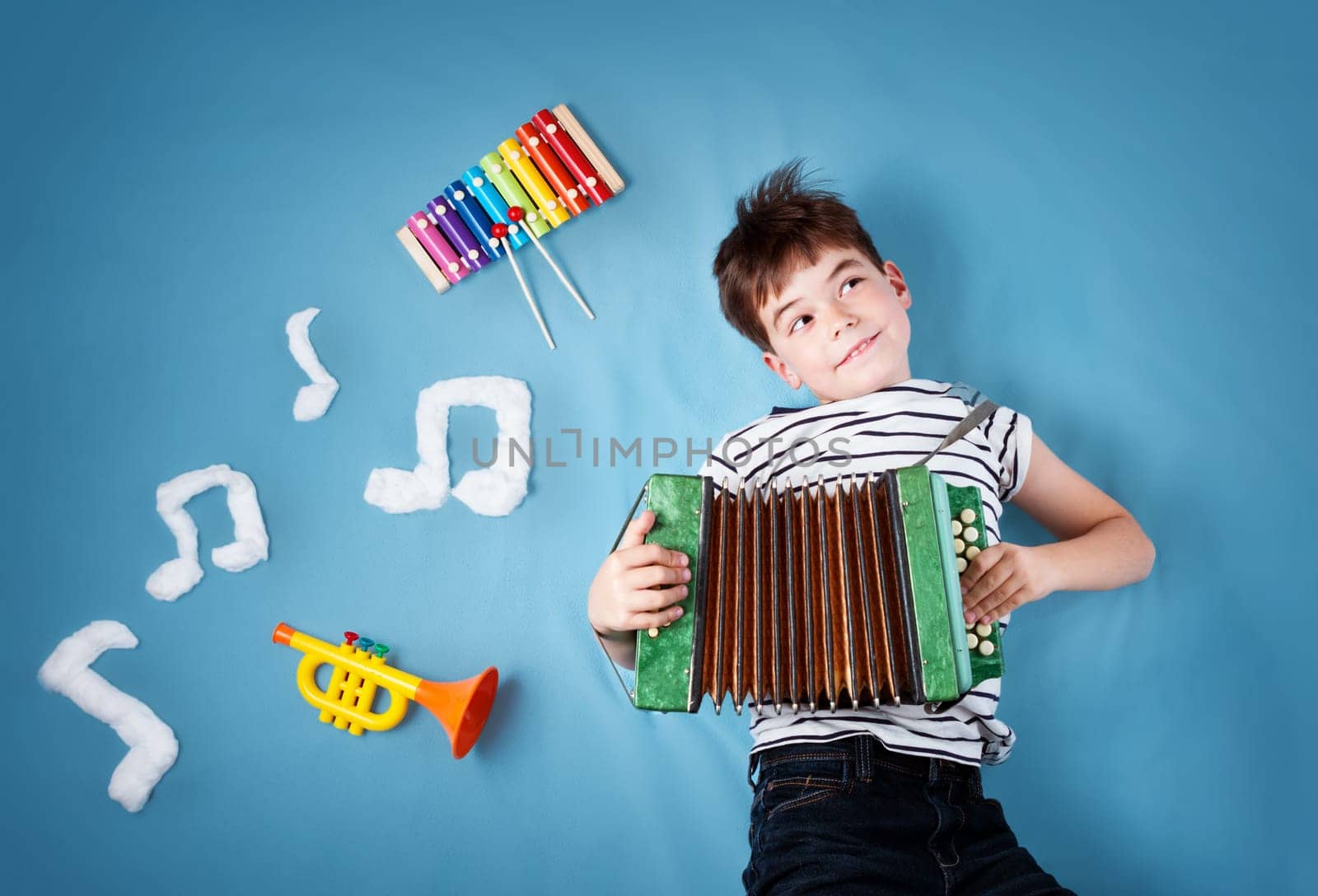 happy seven years old boy on blue blanket background with accordion and musical notes. Young child singing song