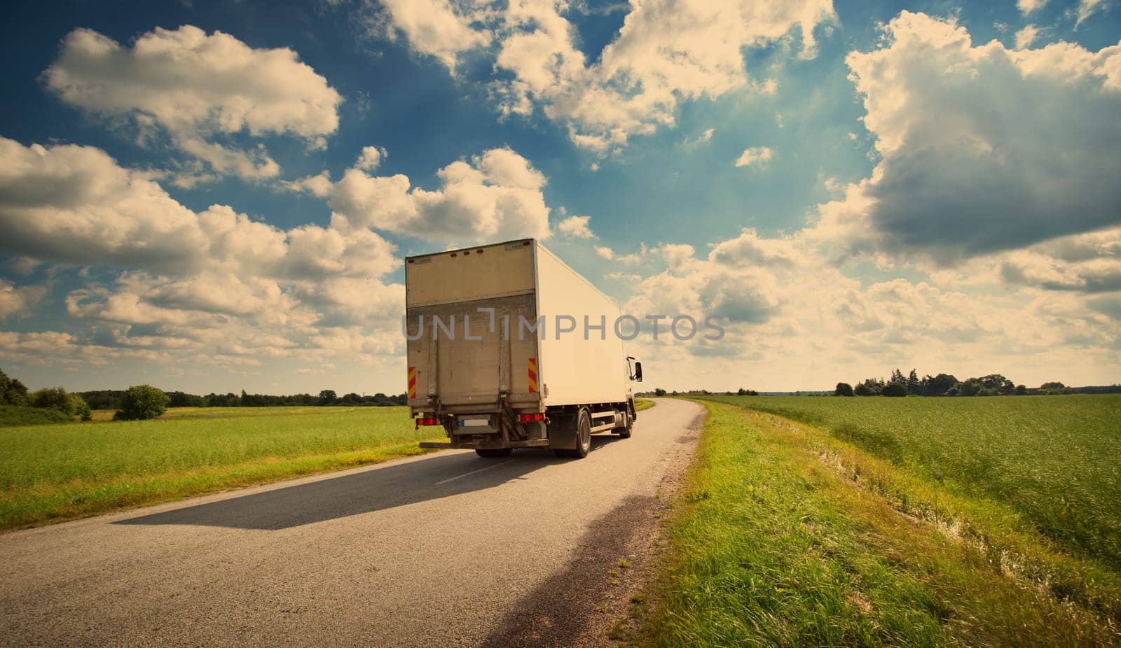 asphalt road on dandelion field with a small truck. lorry moving on sunny evening