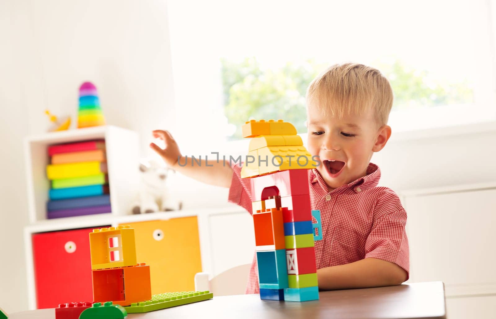 Little child playing with blocks. Boy sitting on the chair at table and building a house