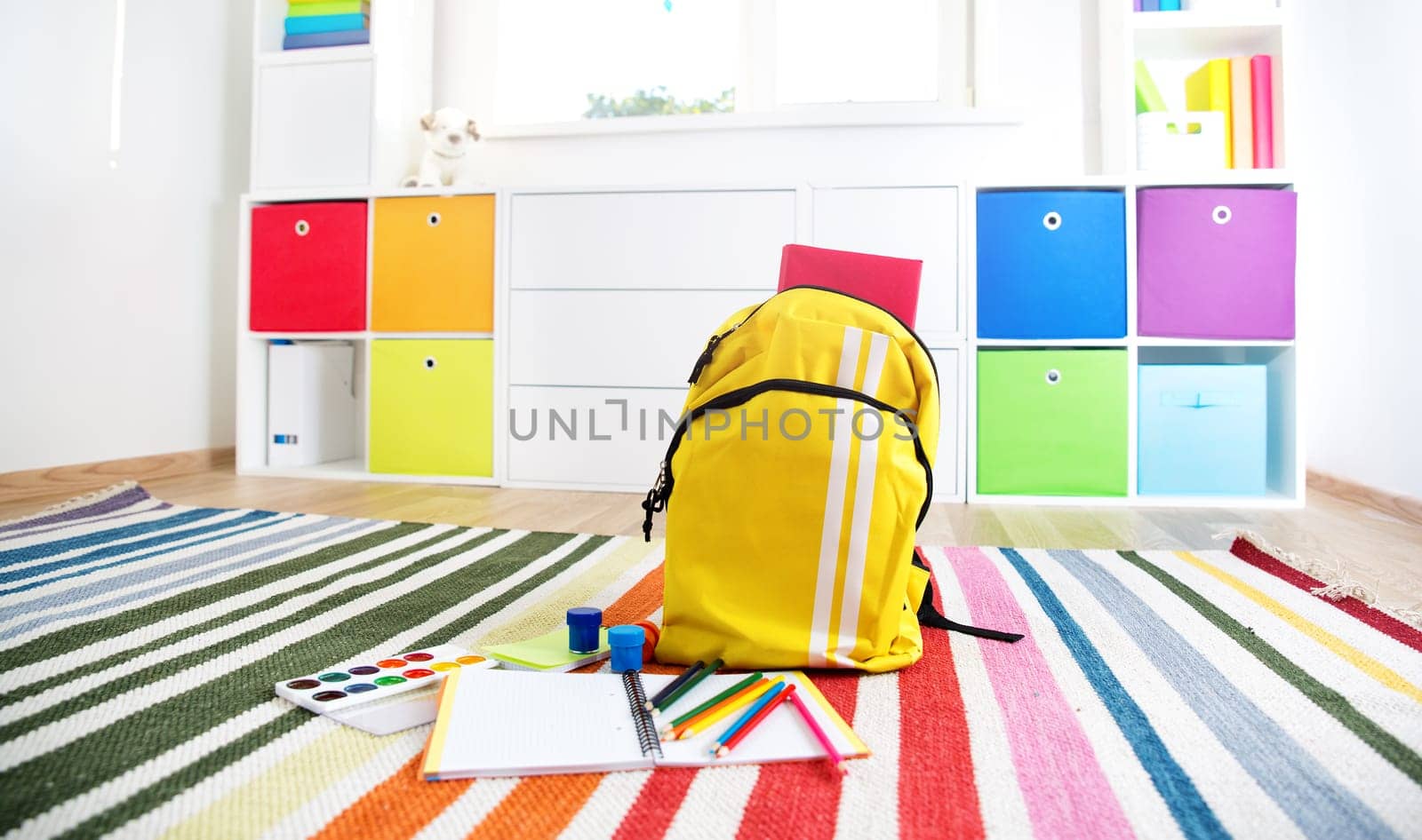 Colourful children rooom with white walls and furniture. Rainbow carpet at home interior with a window