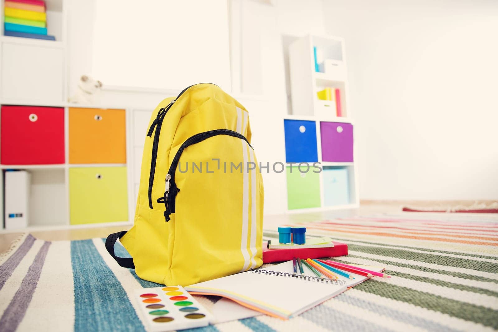 Colourful children rooom with white walls and furniture. Rainbow carpet at home interior with a window
