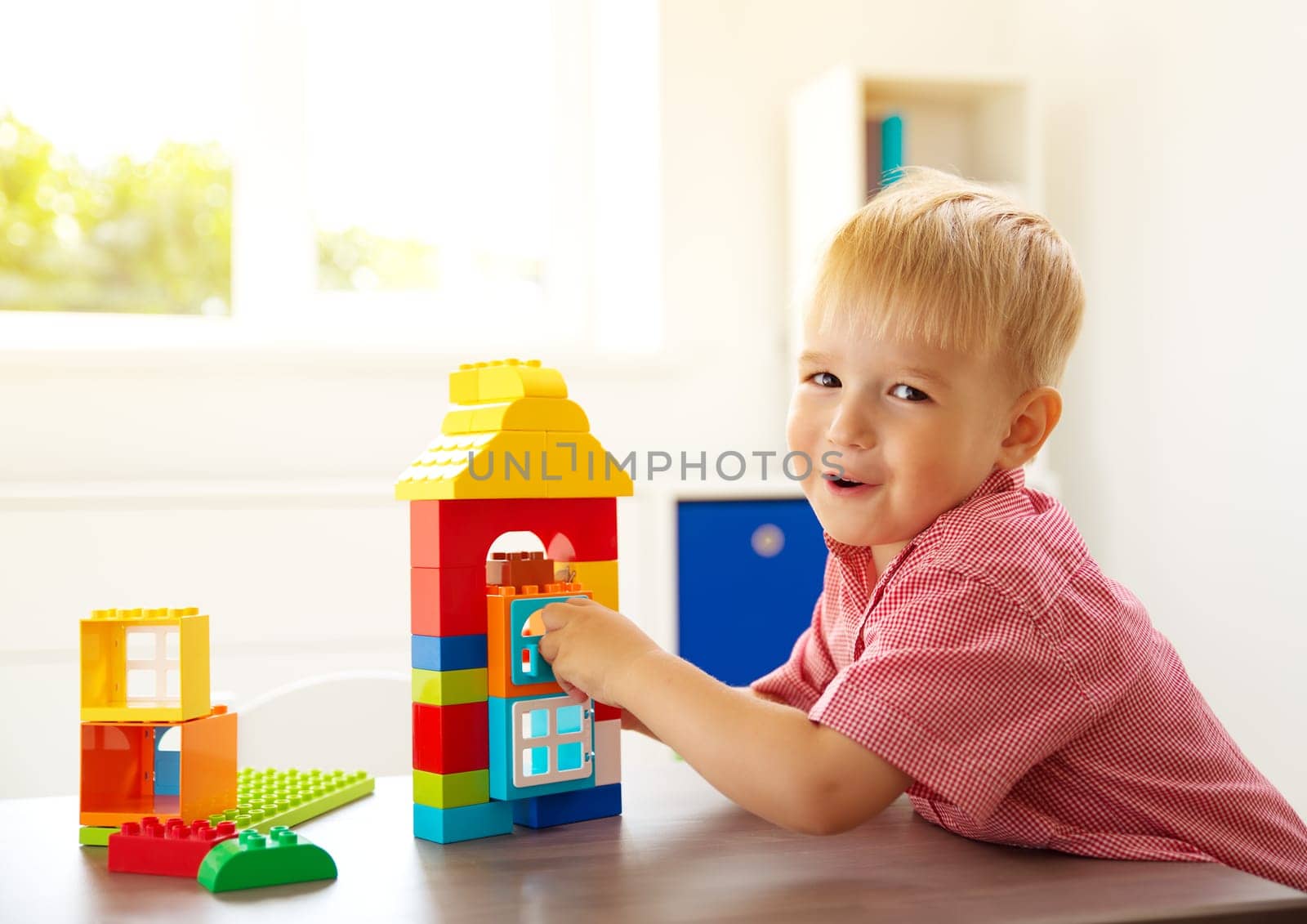 Little child playing with blocks. Boy sitting on the chair at table and building a house
