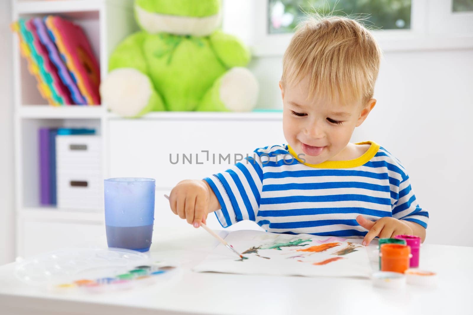Little child drawing on the paper. Boy sitting on the chair at table with paints