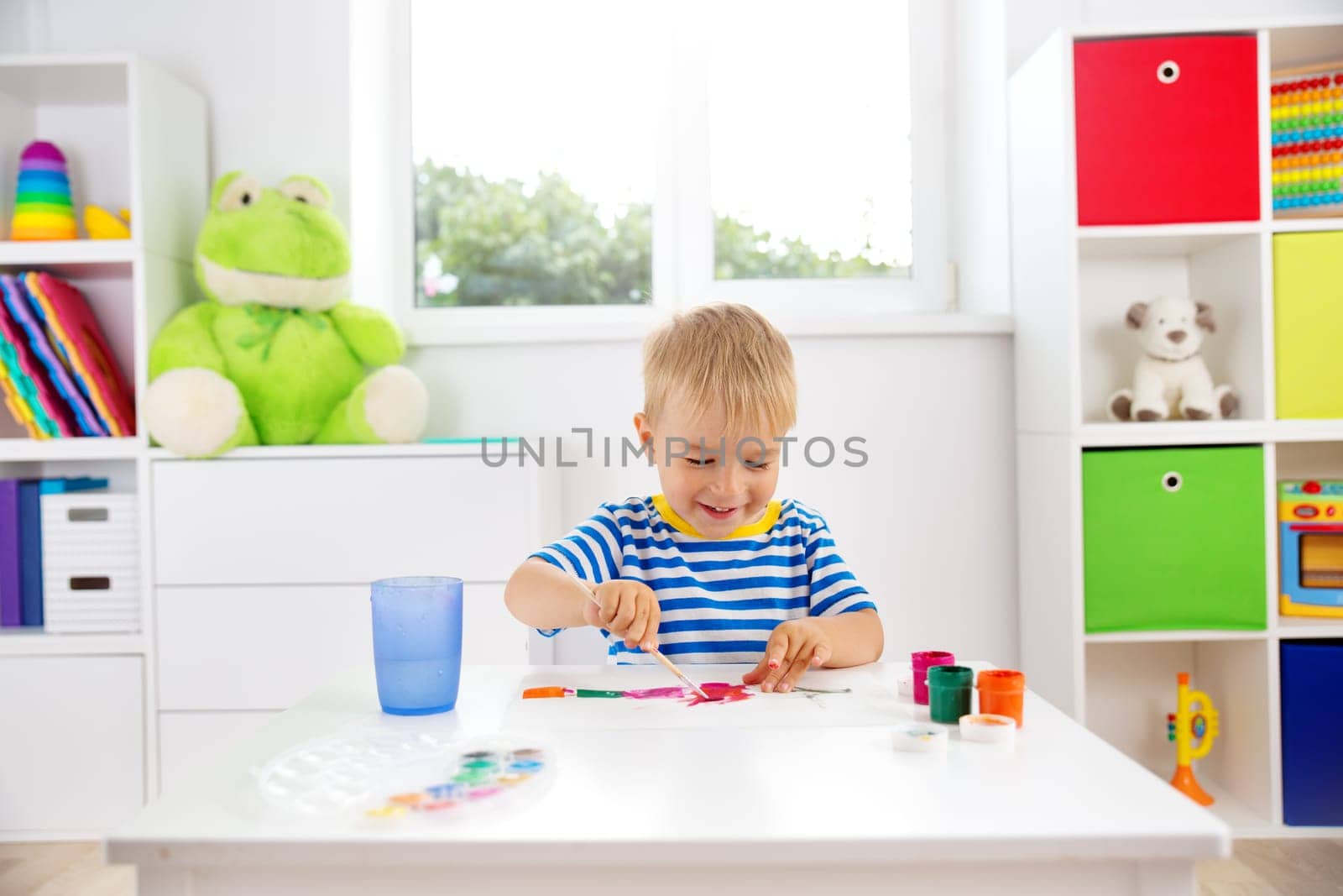 Little child drawing on the paper. Boy sitting on the chair at table with paints
