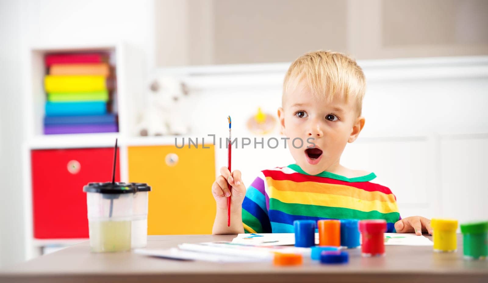 Little child drawing on the paper. Boy sitting on the chair at table with paints
