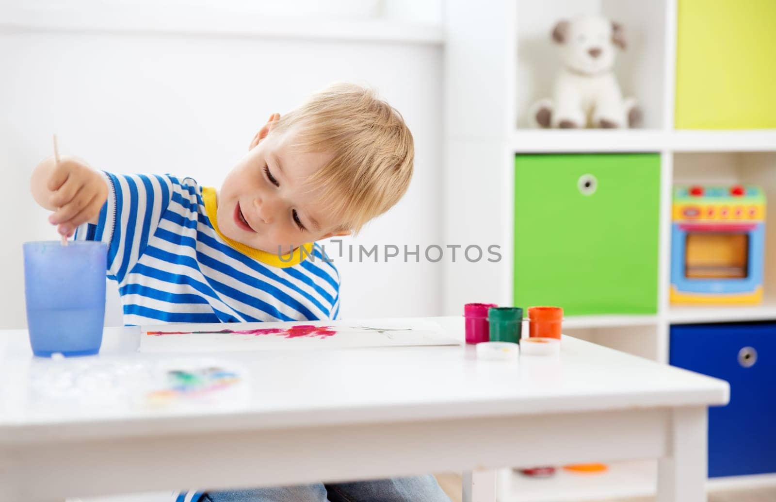 Little child drawing on the paper. Boy sitting on the chair at table with paints