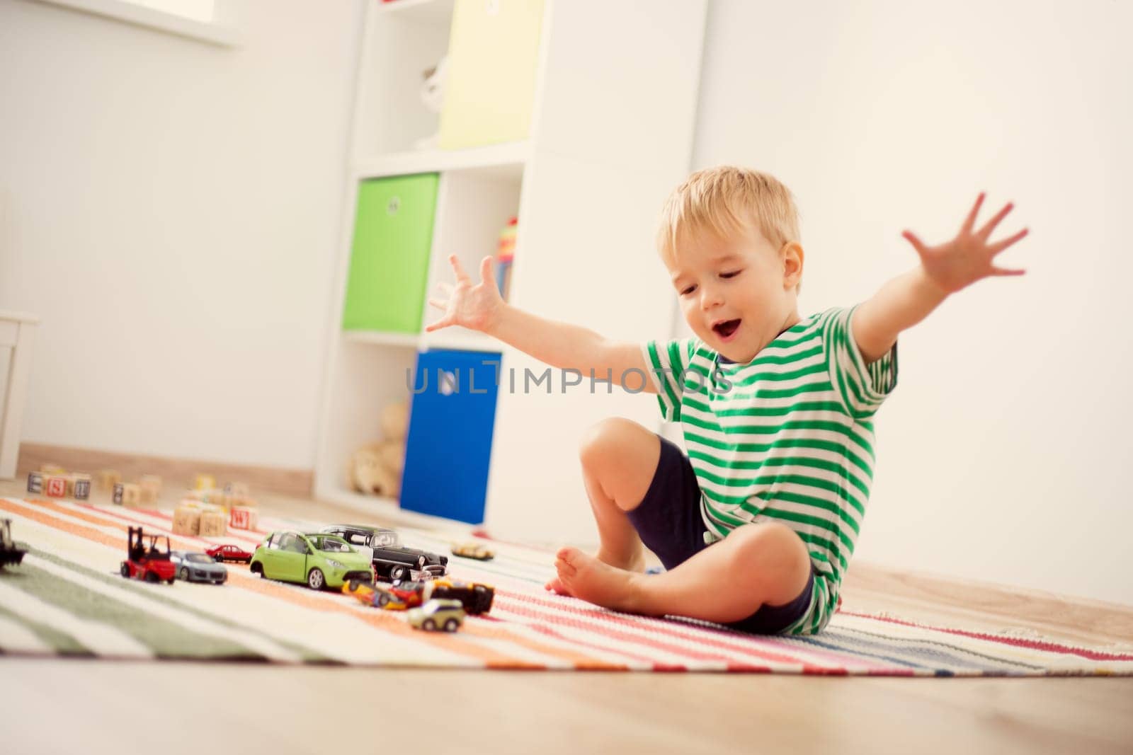 Little child playing with toy cars. Boy sitting on the floor at home