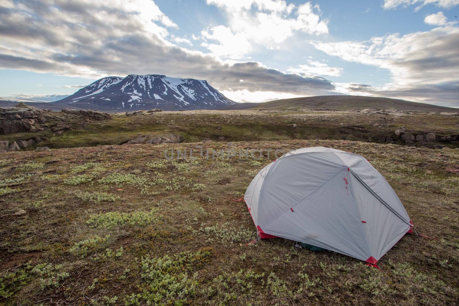 Tent in Icelandic nature with snow covered hill and blue sky with clouds. Concept of adventure on travels in Scandinavian nature. Wide angle of camping in wilderness with copy space.