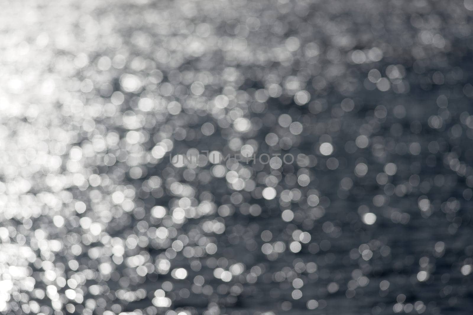 7 - Extra large white circular bokeh, formed by looking into the sun hitting water ripples on an outdoor reservoir lake. Abstract plain background.